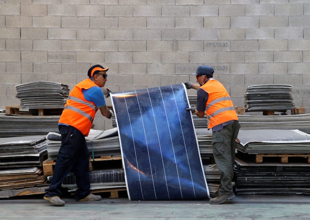 Reciclaje de paneles solares, dos obreros apilando placas fotovoltaicas en el suelo