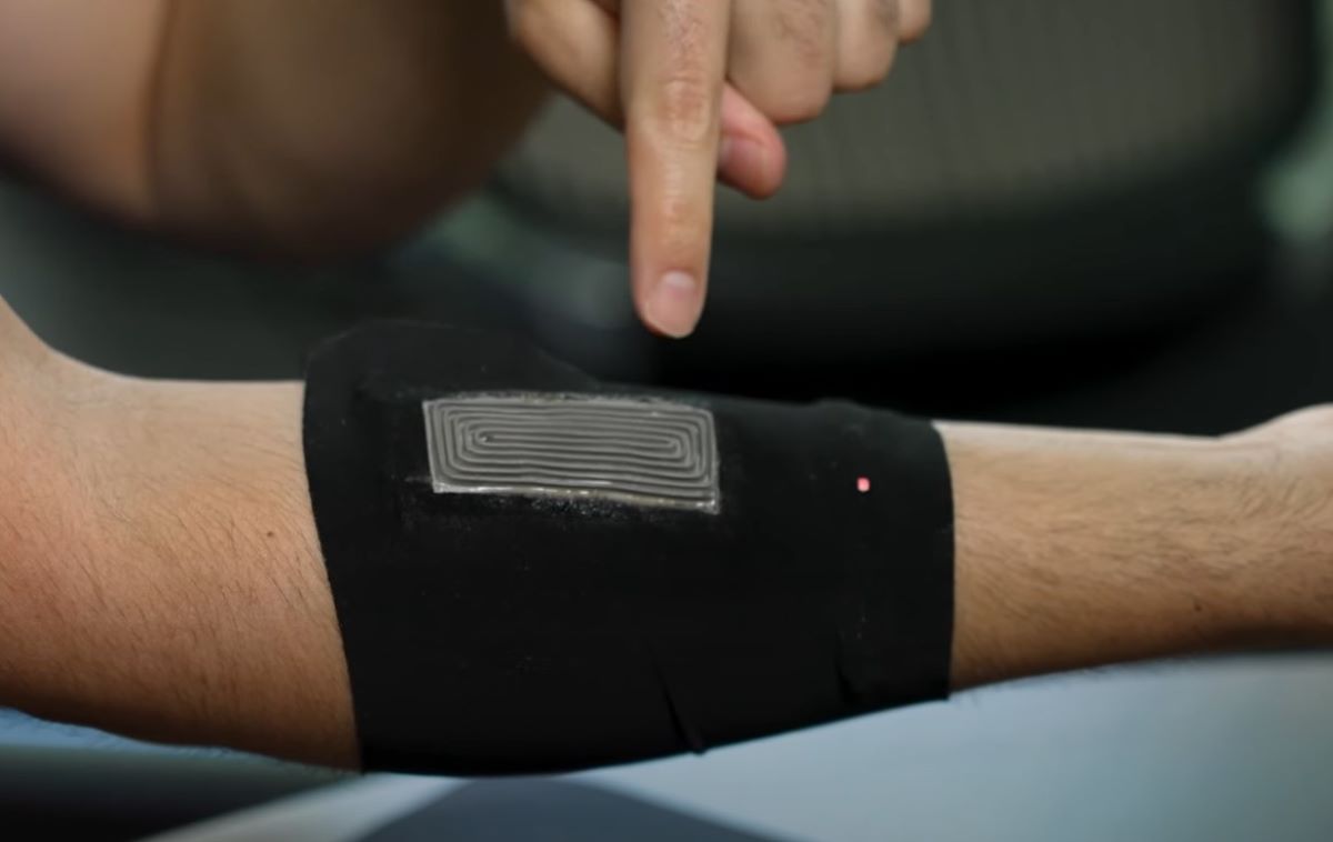 La imagen muestra un dispositivo portátil que se coloca en la piel, probablemente en el brazo, diseñado para aprovechar el calor corporal. La persona está señalando el dispositivo, que parece estar compuesto de varios componentes dispuestos en capas visibles. El dispositivo parece ser flexible y está adherido al cuerpo, lo que coincide con la descripción de un dispositivo termoeléctrico capaz de convertir el calor corporal en energía eléctrica para alimentar pequeños aparatos electrónicos, como un LED, que se puede observar encendido en la parte inferior derecha del dispositivo.

Este tipo de dispositivo está alineado con tecnologías avanzadas en el campo de la sostenibilidad, donde se busca aprovechar fuentes de energía alternativas como el calor corporal para alimentar dispositivos sin la necesidad de baterías tradicionales.