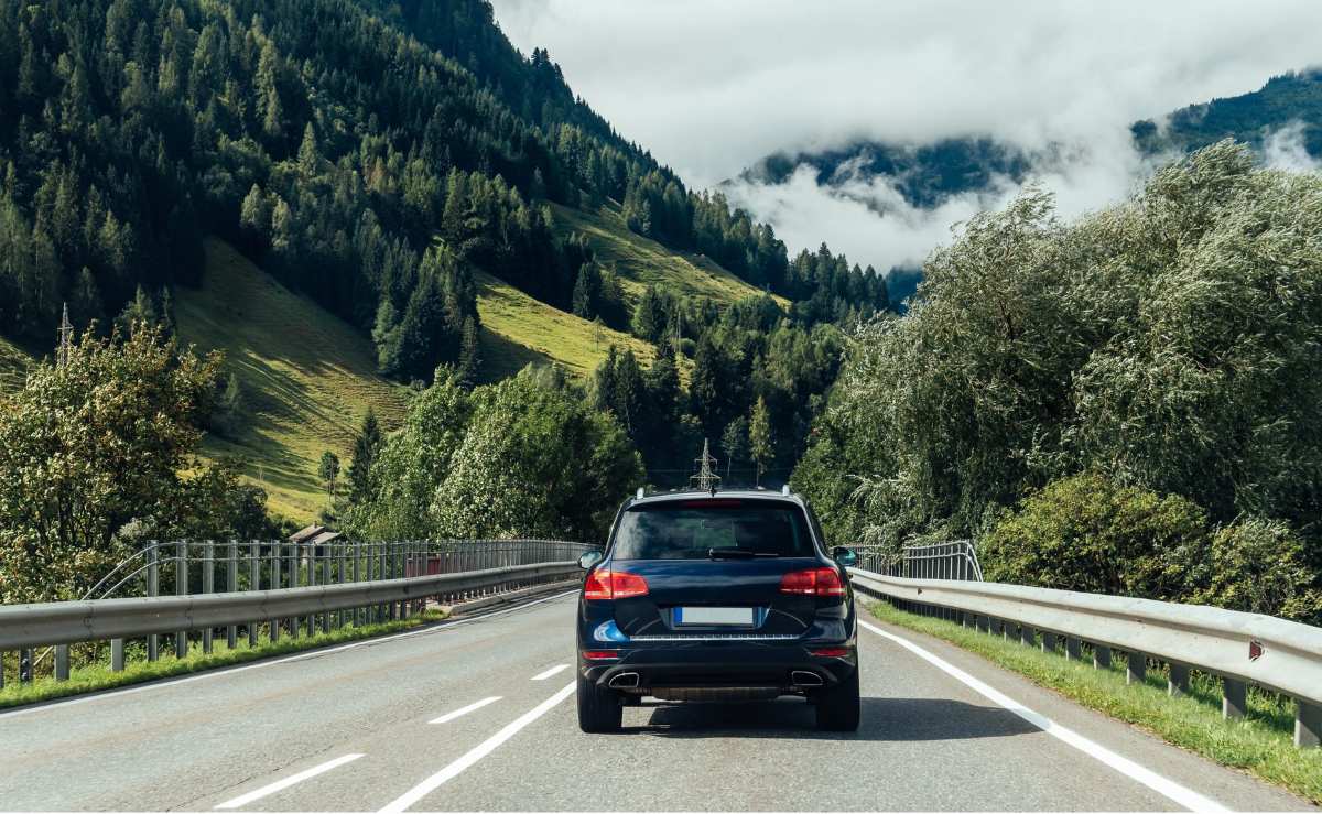 La imagen muestra un vehículo eléctrico viajando por una carretera rodeada de un exuberante paisaje verde en Noruega, con colinas cubiertas de árboles y nubes bajas en el horizonte. Este escenario refleja la armonía entre la infraestructura moderna de transporte sostenible y la naturaleza característica de Noruega. El país es conocido por su liderazgo en la adopción de vehículos eléctricos, integrando movilidad ecológica en entornos rurales y urbanos.